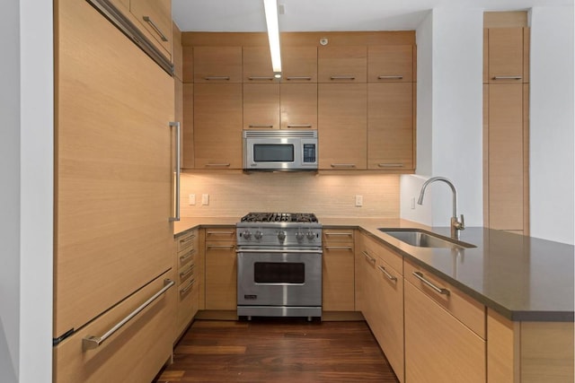 kitchen with high end appliances, kitchen peninsula, light brown cabinets, and sink