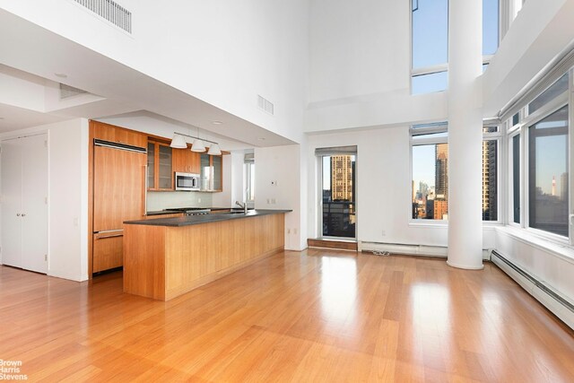 kitchen with kitchen peninsula, decorative light fixtures, a kitchen breakfast bar, light hardwood / wood-style floors, and baseboard heating