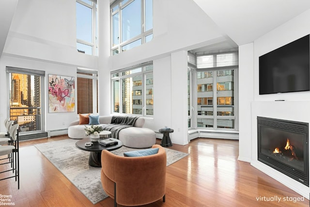 living room with a baseboard heating unit, hardwood / wood-style flooring, and a towering ceiling