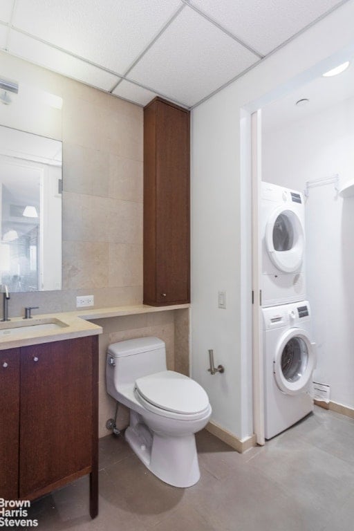 bathroom with stacked washing maching and dryer, vanity, toilet, a drop ceiling, and tile patterned floors