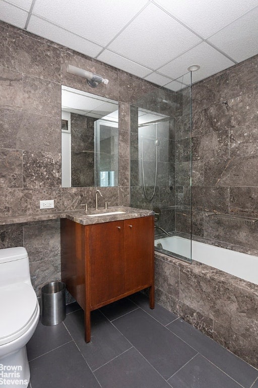 full bathroom with tile patterned floors, toilet, tiled shower / bath combo, and tile walls