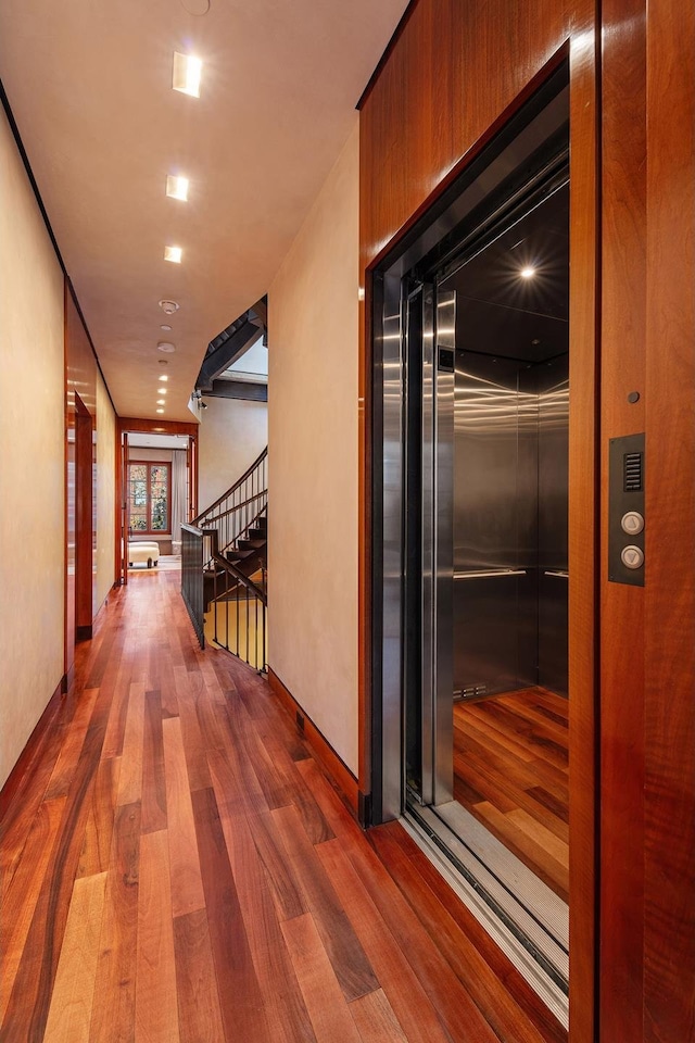 hall featuring baseboards, elevator, wood finished floors, and stairs