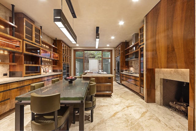 kitchen with brown cabinets, a center island with sink, and open shelves