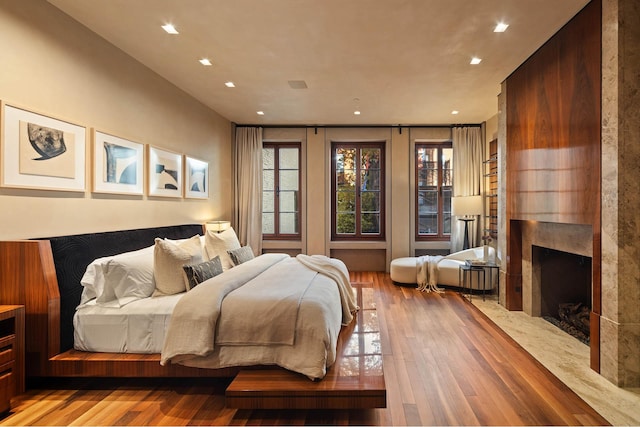bedroom with light wood-style floors, a high end fireplace, recessed lighting, and multiple windows