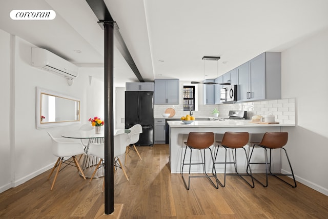 kitchen with kitchen peninsula, appliances with stainless steel finishes, gray cabinetry, a wall mounted air conditioner, and a breakfast bar