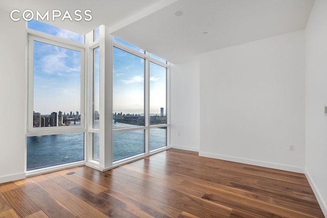 spare room featuring baseboards, wood-type flooring, a water view, a wall of windows, and a city view