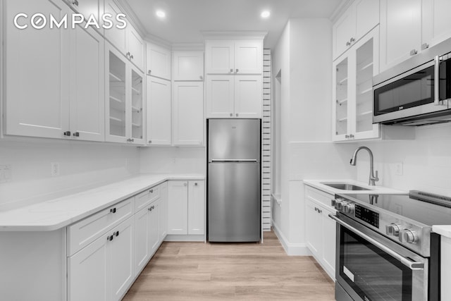 kitchen with a sink, white cabinetry, stainless steel appliances, light wood-style floors, and decorative backsplash