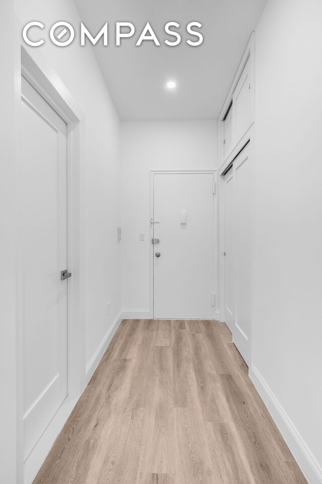 corridor featuring baseboards and light wood finished floors