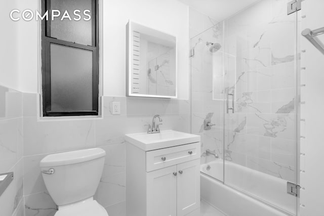 bathroom with tile walls, combined bath / shower with glass door, toilet, and vanity