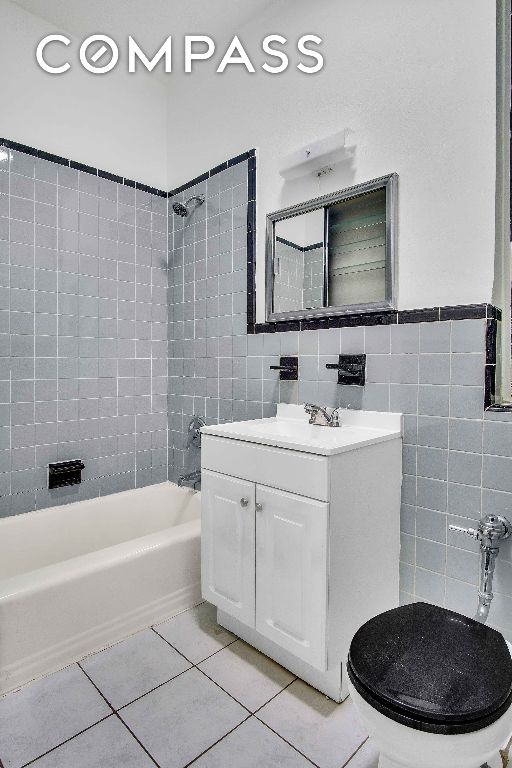 full bathroom with tile walls, tiled shower / bath combo, vanity, tile patterned floors, and toilet