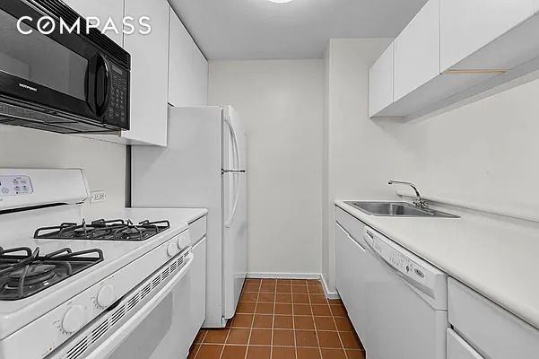 kitchen with white appliances, dark tile patterned flooring, sink, and white cabinets