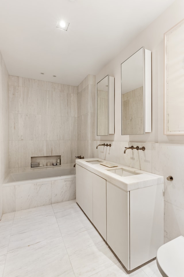 full bath featuring tile walls, a garden tub, double vanity, and a sink