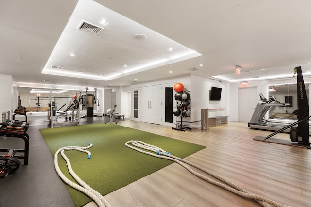 exercise room with recessed lighting, a tray ceiling, visible vents, and wood finished floors