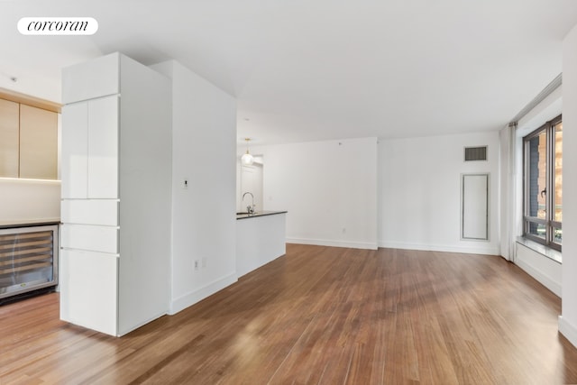 unfurnished living room featuring wine cooler, baseboards, wood finished floors, and visible vents