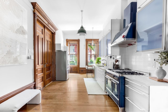 kitchen with light wood-style floors, white cabinets, appliances with stainless steel finishes, wall chimney range hood, and decorative light fixtures