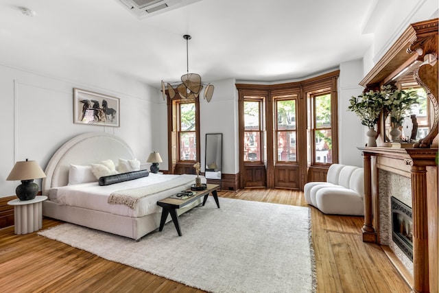 bedroom featuring light wood finished floors, a glass covered fireplace, and visible vents