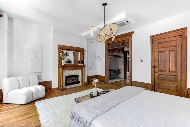 bedroom featuring a chandelier, a glass covered fireplace, a wall unit AC, and wood finished floors