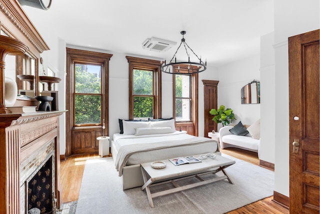 bedroom featuring light wood finished floors, baseboards, a chandelier, and a high end fireplace