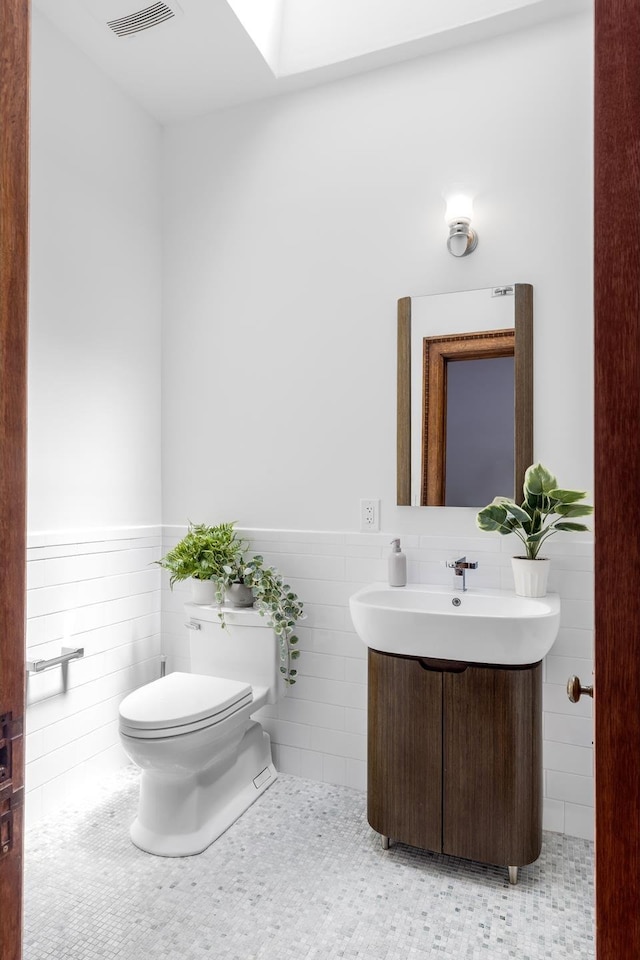 half bathroom featuring tile walls, toilet, wainscoting, vanity, and tile patterned flooring