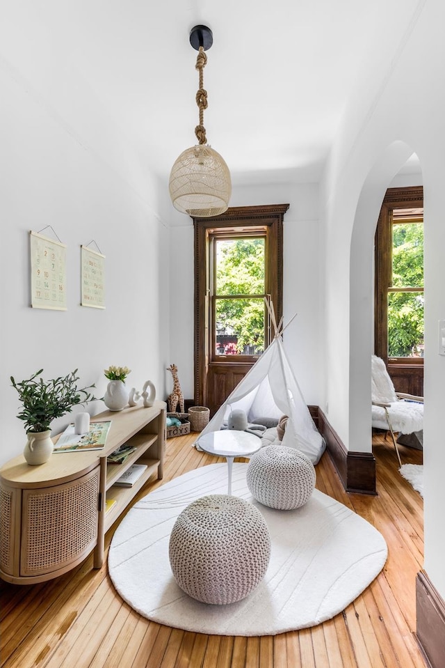 sitting room featuring plenty of natural light, wood-type flooring, arched walkways, and baseboards