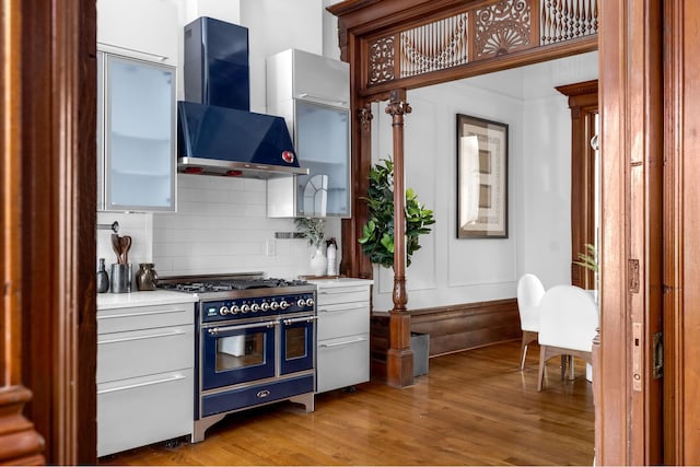 kitchen with range with two ovens, light wood-style floors, light countertops, backsplash, and range hood