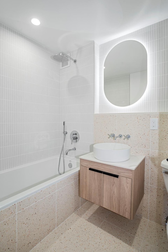 bathroom featuring toilet, tiled shower / bath combo, vanity, tile walls, and recessed lighting