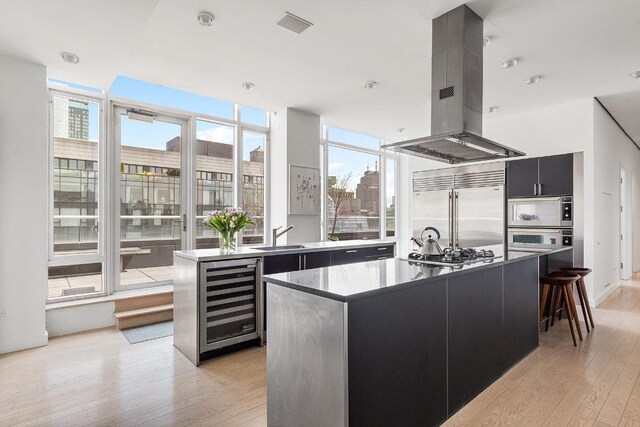 kitchen featuring beverage cooler, dark cabinets, a center island, built in appliances, and island exhaust hood