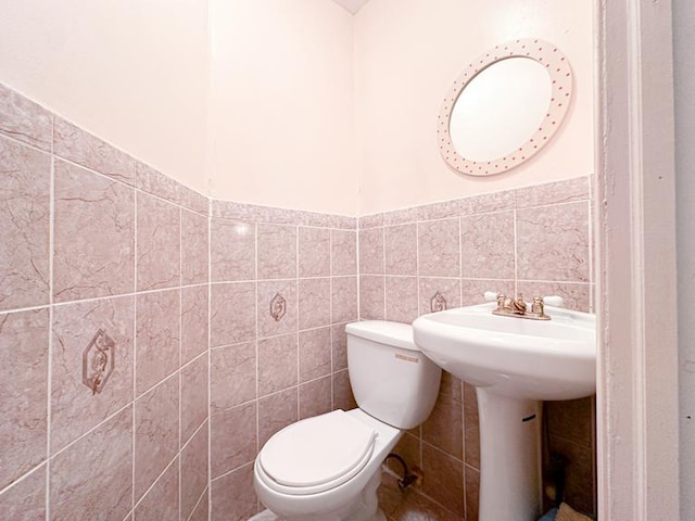 half bath featuring a wainscoted wall, a sink, toilet, and tile walls