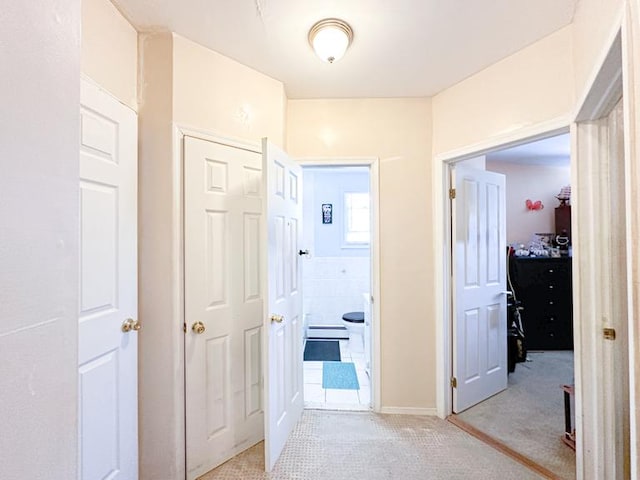 hall featuring a baseboard heating unit, light carpet, and tile walls