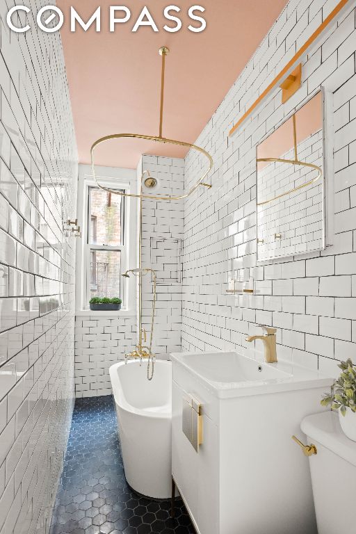 bathroom featuring toilet, tile patterned flooring, tile walls, a tub, and sink