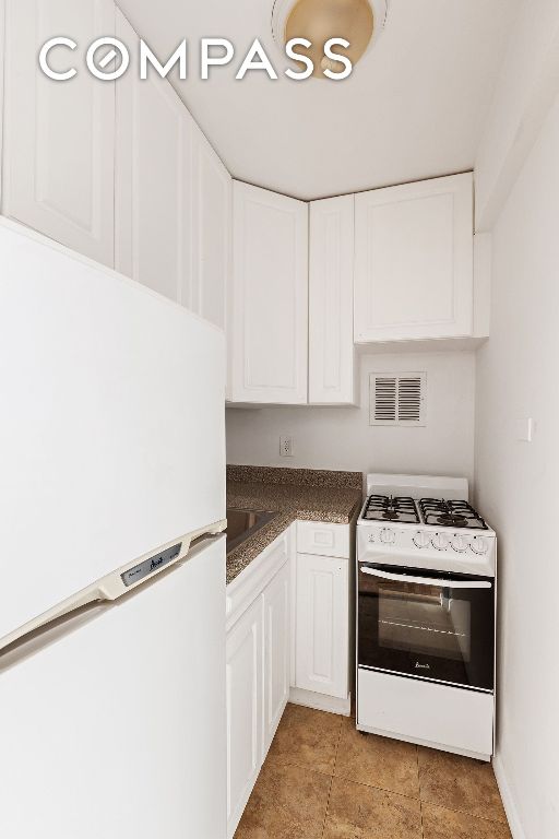 kitchen featuring dark countertops, visible vents, white cabinetry, white appliances, and baseboards