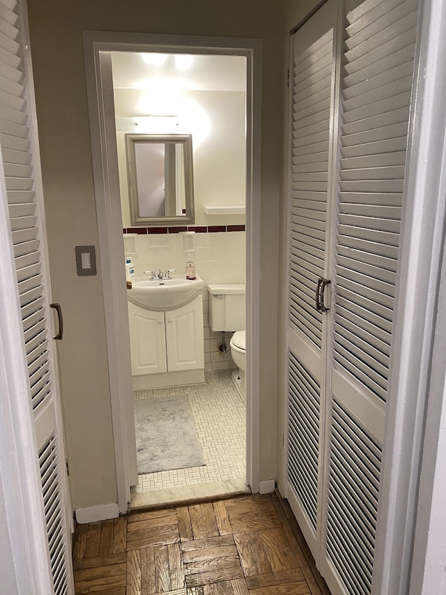 half bath featuring vanity, tile walls, toilet, and wainscoting