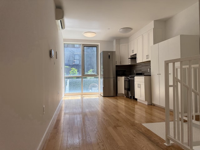 362 W 127th St Unit 1-A, New York City, NY 10027 - kitchen with freestanding refrigerator, black range with electric cooktop, under cabinet range hood, a wall unit AC, and wood finished floors