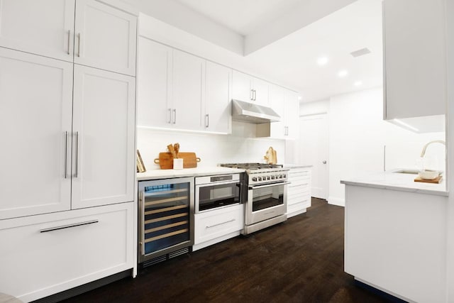 kitchen with sink, high end stainless steel range oven, white cabinets, dark hardwood / wood-style flooring, and beverage cooler