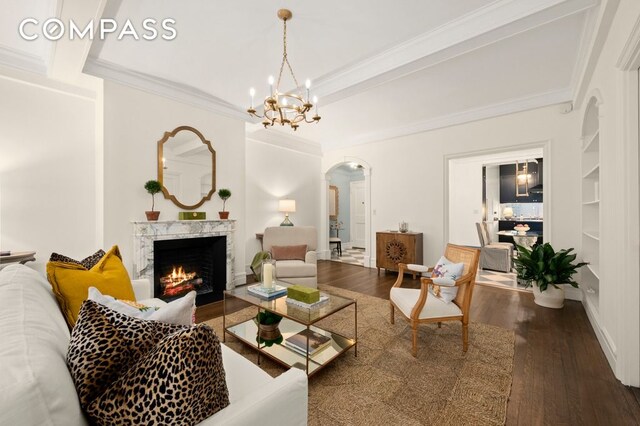 living room featuring dark hardwood / wood-style floors, built in features, ornamental molding, a notable chandelier, and a high end fireplace