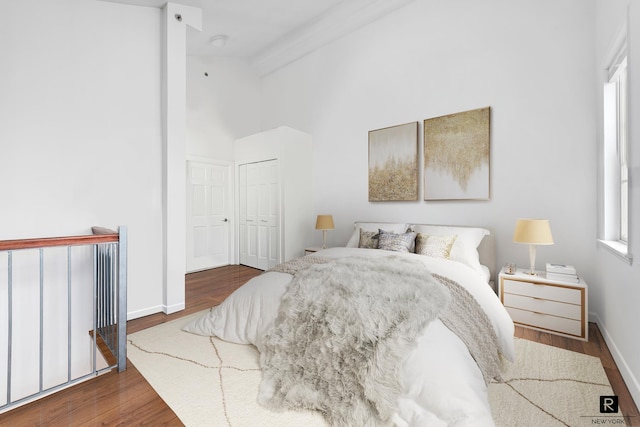 bedroom featuring high vaulted ceiling, a closet, baseboards, and wood finished floors