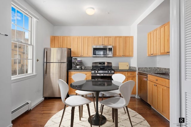 kitchen with appliances with stainless steel finishes, a baseboard heating unit, dark wood-type flooring, dark stone counters, and light brown cabinets