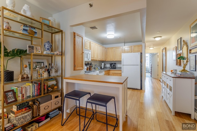 kitchen with white appliances, a peninsula, light brown cabinets, and light wood finished floors