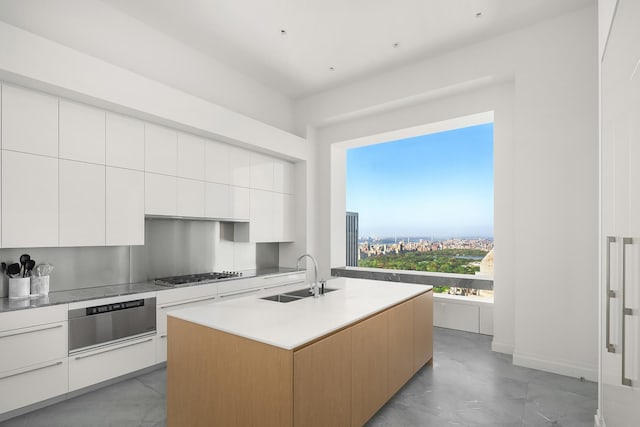 kitchen with a sink, modern cabinets, gas stovetop, white cabinetry, and a kitchen island with sink