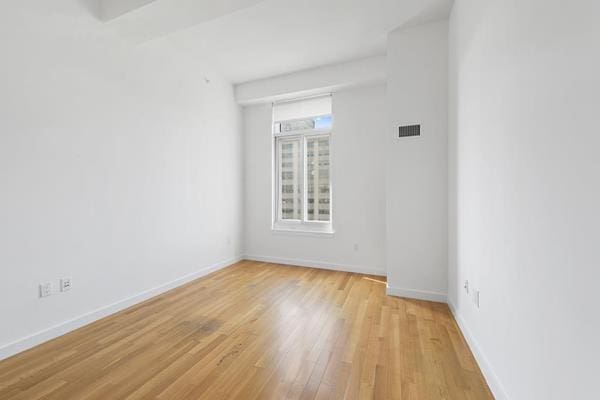 empty room with light wood finished floors, visible vents, and baseboards