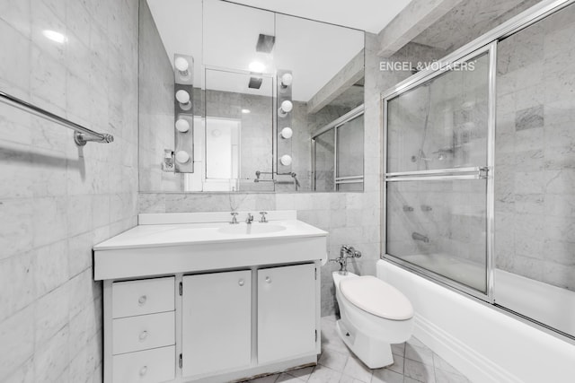 bathroom with tile walls, vanity, toilet, combined bath / shower with glass door, and tile patterned flooring