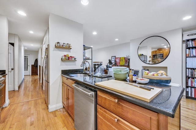 kitchen with appliances with stainless steel finishes, sink, dark stone countertops, and light wood-type flooring