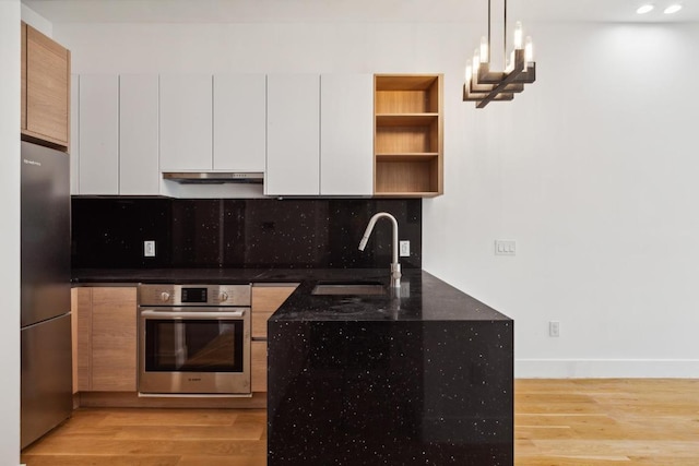 kitchen featuring hanging light fixtures, stainless steel fridge, wall oven, white cabinets, and sink