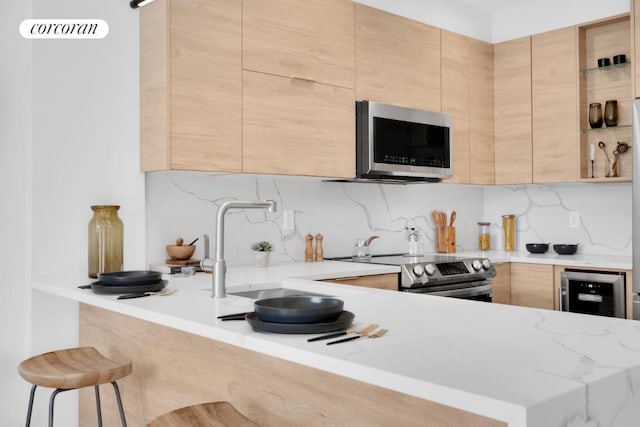 kitchen featuring stainless steel appliances, a kitchen breakfast bar, light stone counters, light brown cabinetry, and kitchen peninsula