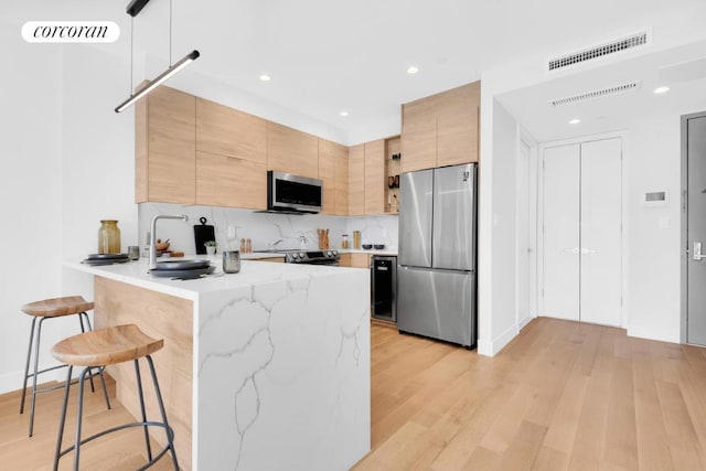 kitchen featuring appliances with stainless steel finishes, a breakfast bar area, kitchen peninsula, light stone countertops, and light hardwood / wood-style flooring