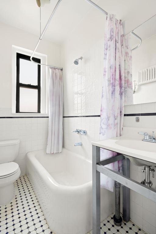 bathroom featuring a wainscoted wall, shower / tub combo with curtain, tile walls, and toilet