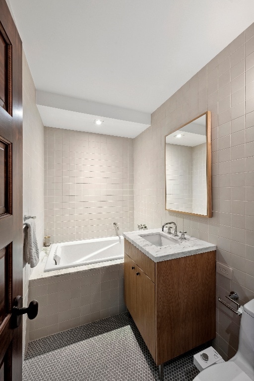 bathroom with tile walls, vanity, toilet, tiled tub, and tile patterned floors