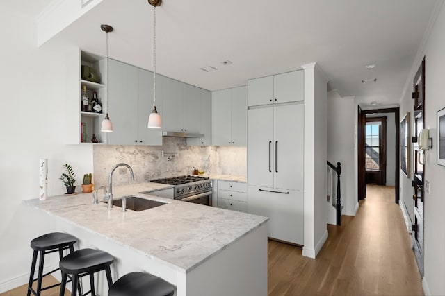 kitchen featuring a kitchen bar, sink, high end appliances, hanging light fixtures, and kitchen peninsula