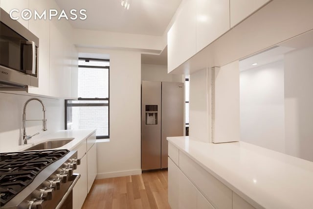 kitchen with light wood finished floors, stainless steel appliances, light countertops, white cabinetry, and a sink