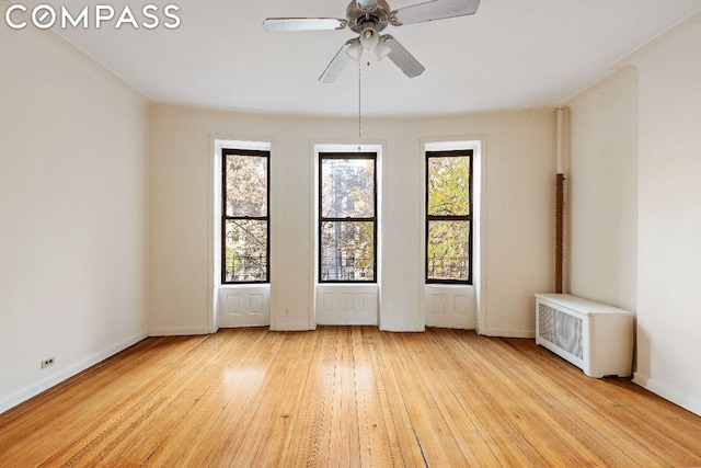 unfurnished room with radiator, plenty of natural light, ceiling fan, and light wood-type flooring